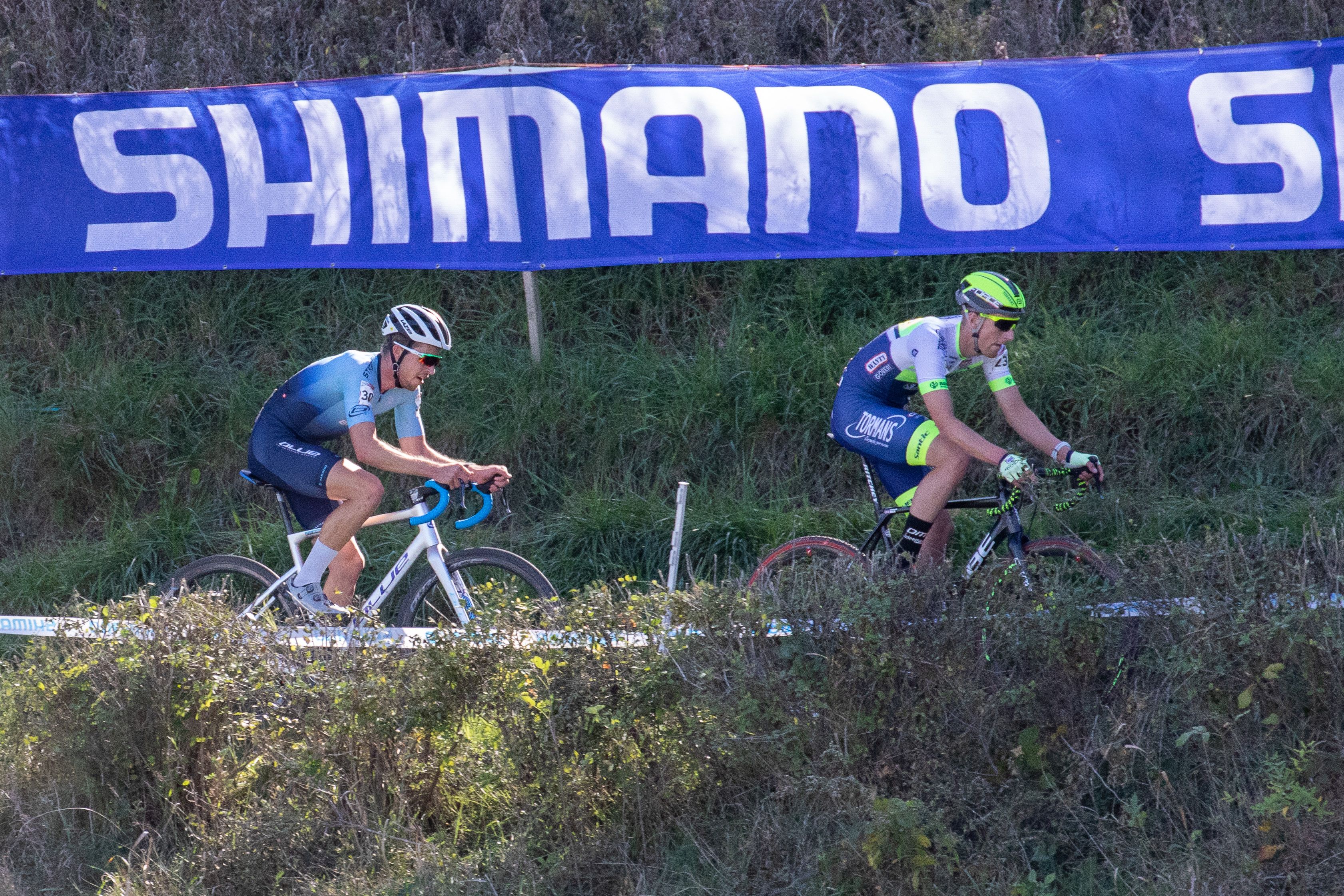 Cyclocross Racers riding with Shimano Banner behind them. 