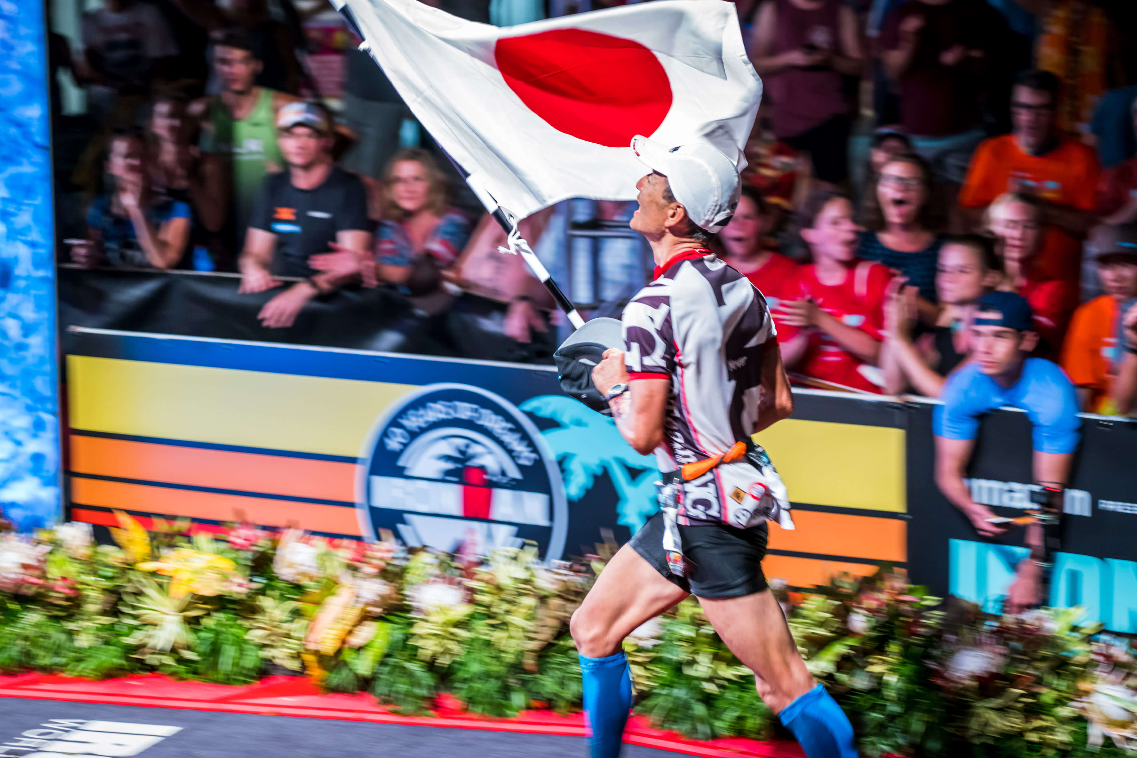 Man running across finishline with Japanese flag at Kona IRONMAN